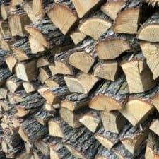 Winnipeg Firewood’s stacked firewood logs—cut with the bark intact and arranged in a neat pile—display both the natural cross-sections of the wood and its rugged outer surfaces.